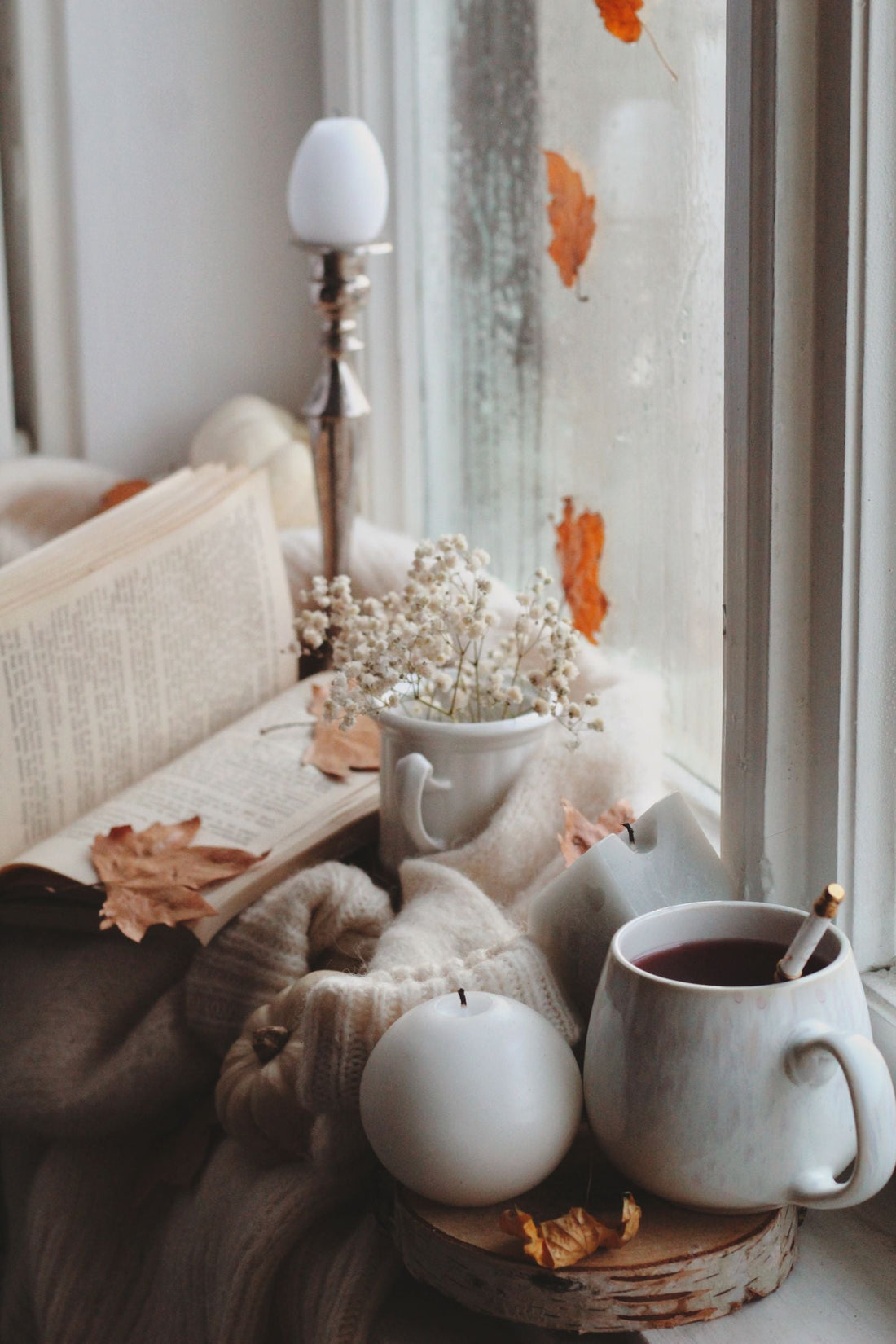 A comforting autumn evening setting with warm tea, candlelight, and a cozy window